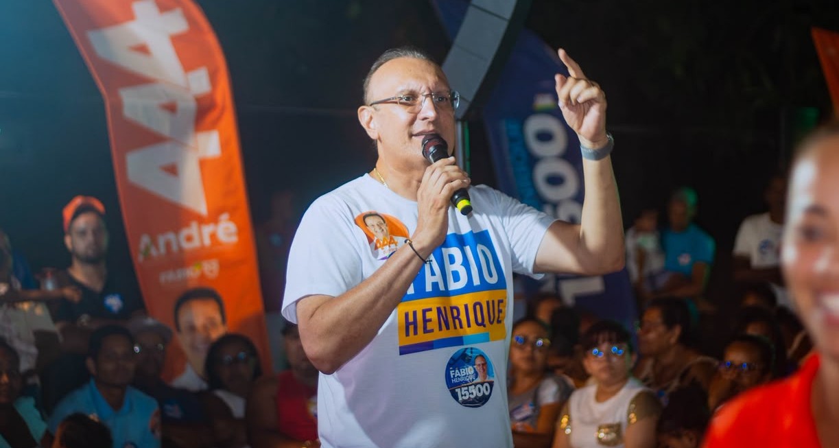 Fábio Henrique discursa ao microfone durante comício noturno, com bandeiras de campanha ao fundo
